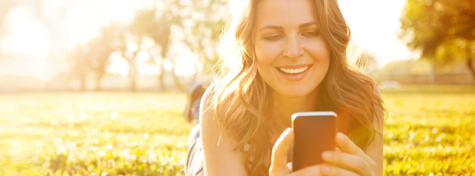 Person laying in a field looking at a phone.