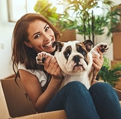 woman holding bulldog puppy in a moving box surrounded by boxes